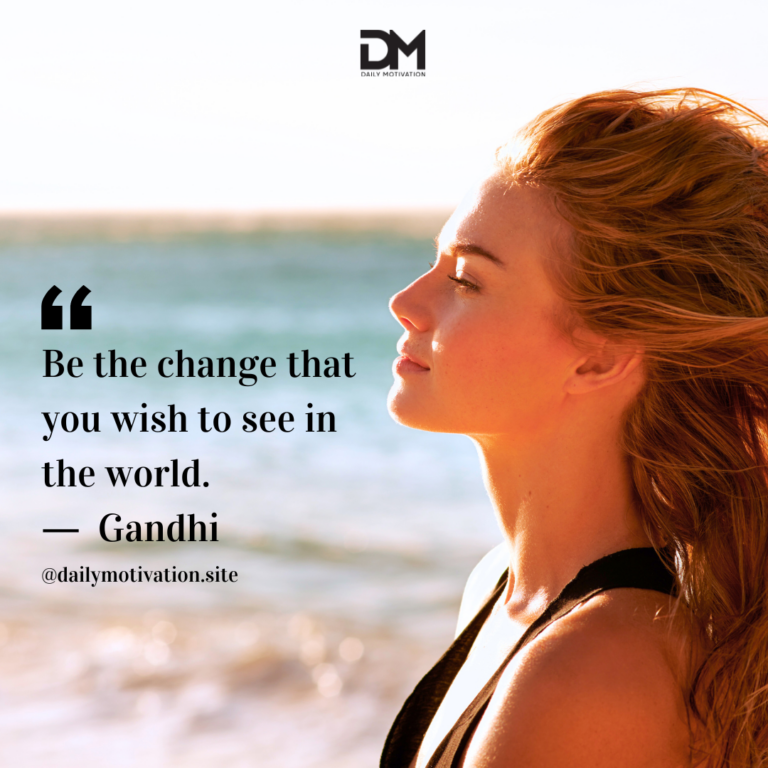 A woman stands on a beach with her hair blowing out behind her in the breeze.