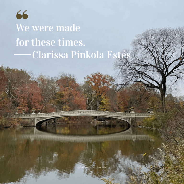 A long bridge over calm water lined by autumn colored trees.