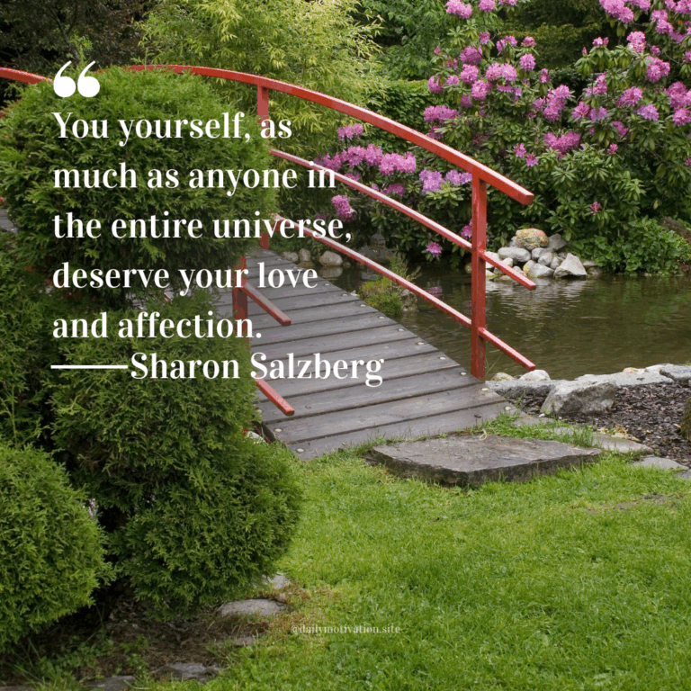 Red footbridge over a calm pond surrounded by lush green grass and blooming pink flowers.