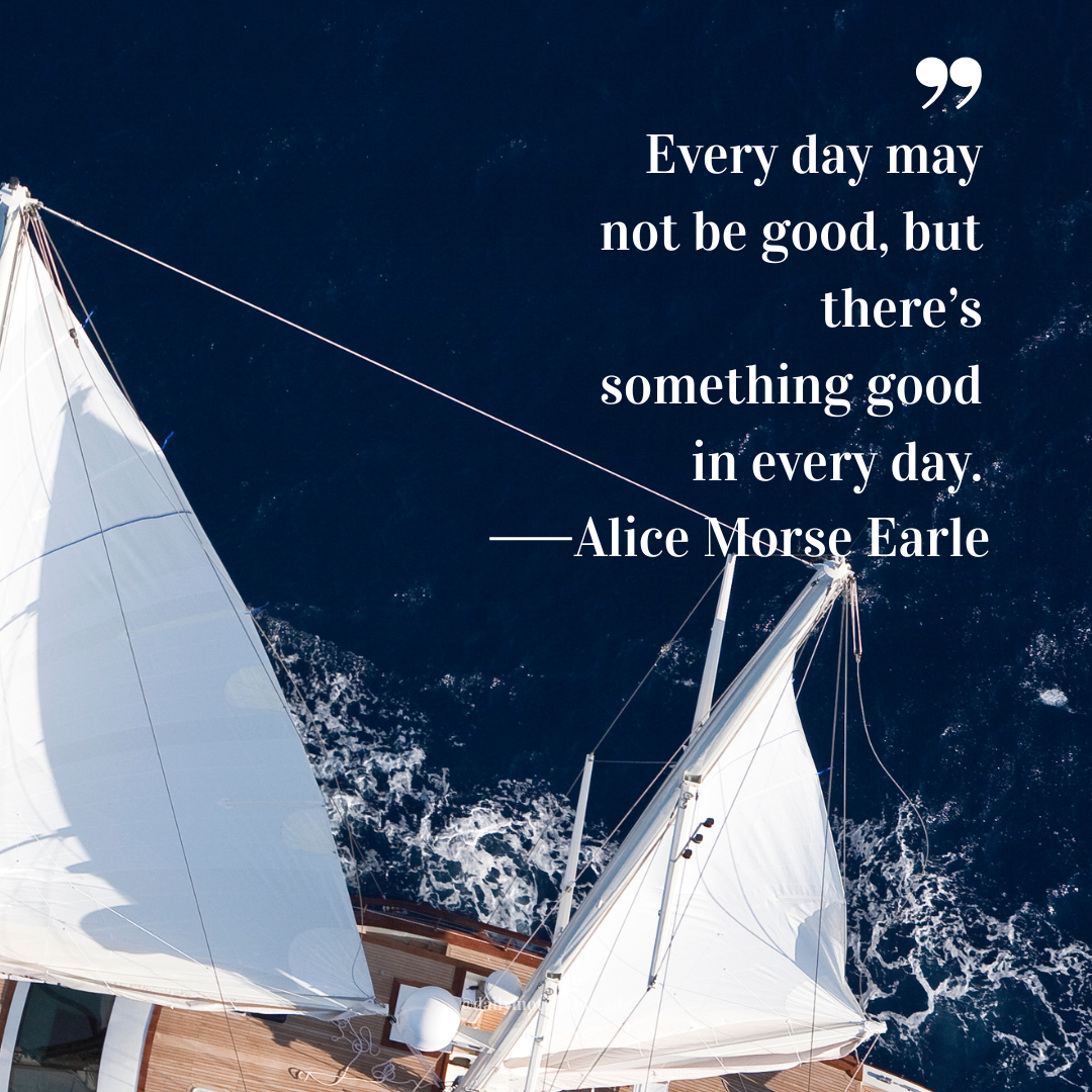 Overhead view of a sailboat cutting through deep blue ocean water with white sails catching the wind.